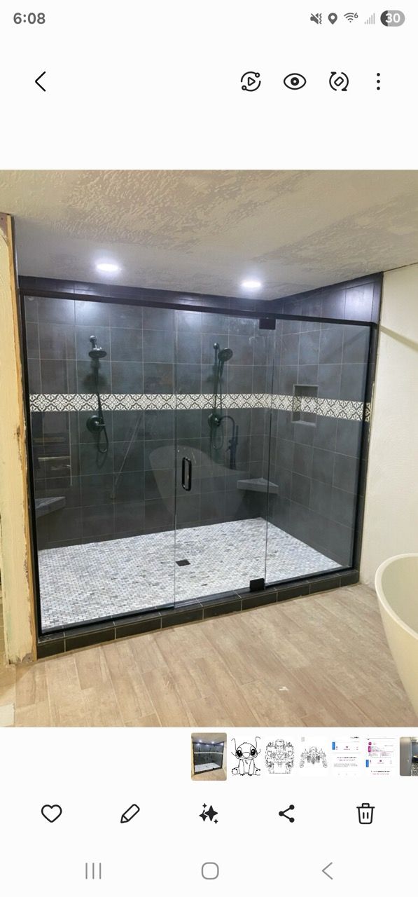 Modern bathroom with a glass shower enclosure, dark tile walls, and white pebble shower floor.