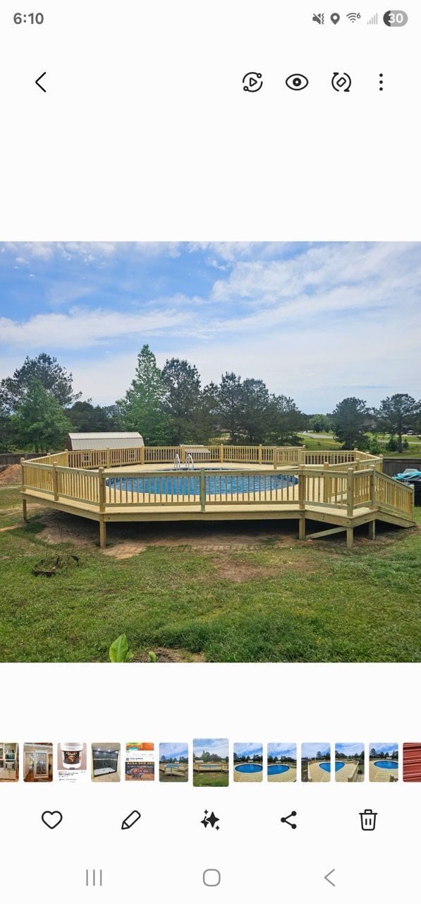 Circular wooden deck in a grassy field under a cloudy blue sky, with trees in the background