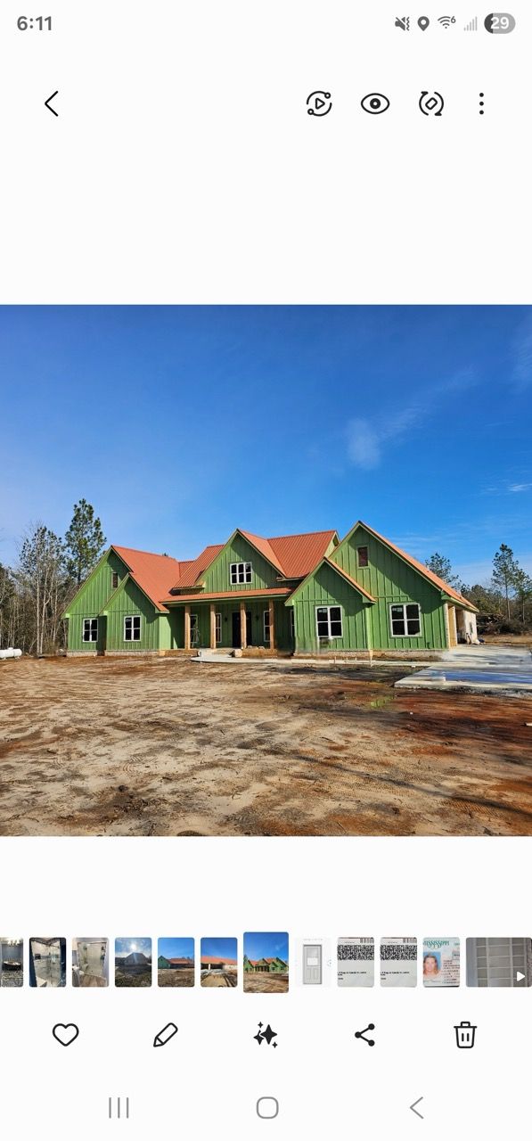 Partially built green house with red roof trusses on a dirt lot under a blue sky