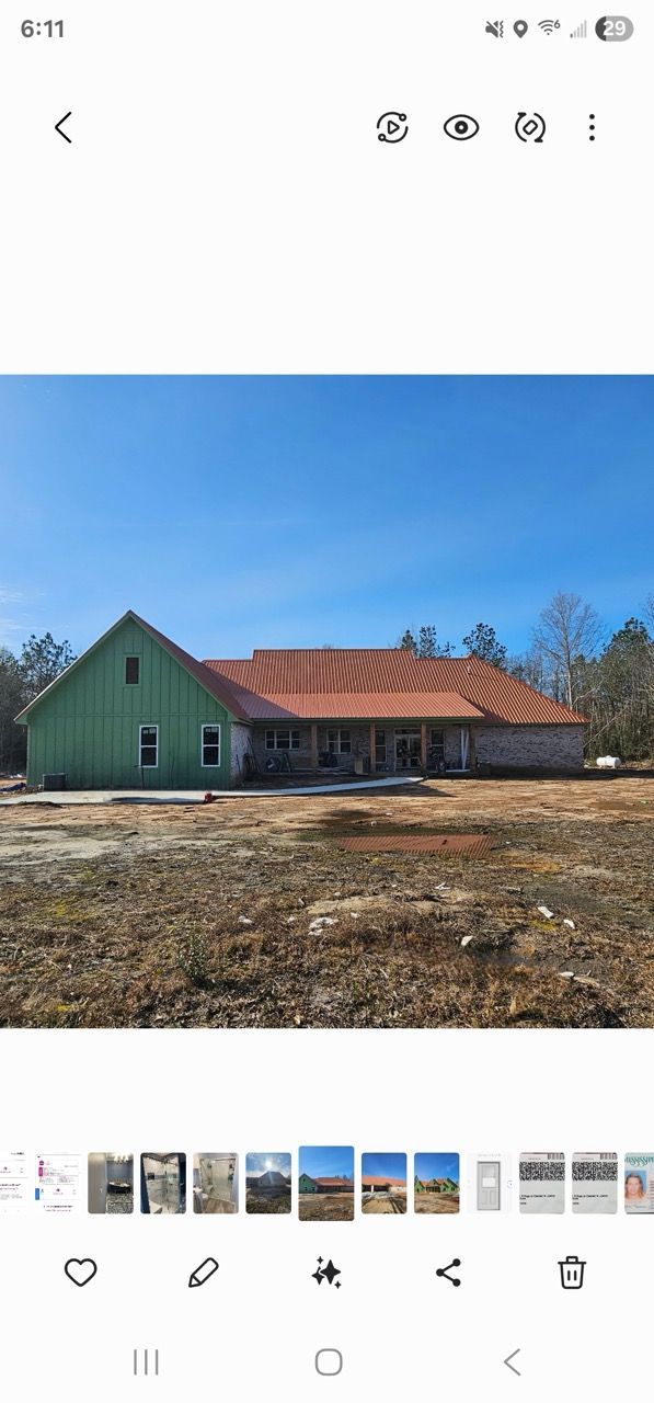 Green house with red-tiled roof under construction on a cleared lot, under a blue sky