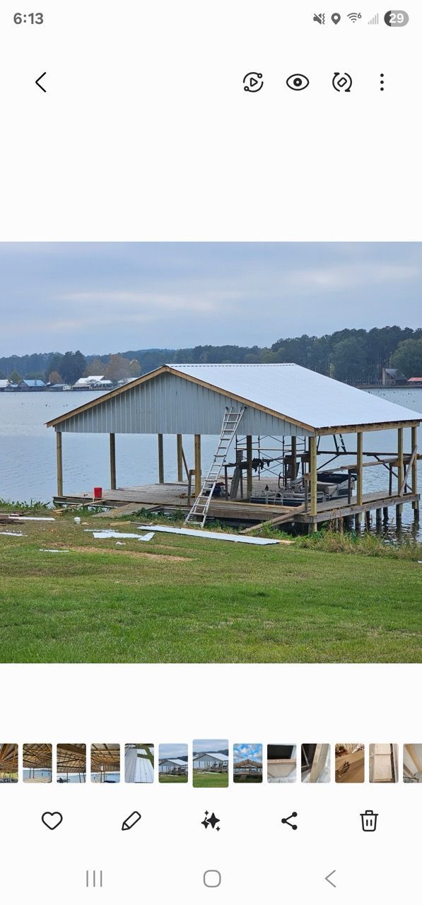 Riverside dock with a roofed wooden shelter, overlooking calm water and distant hills under a cloudy sky