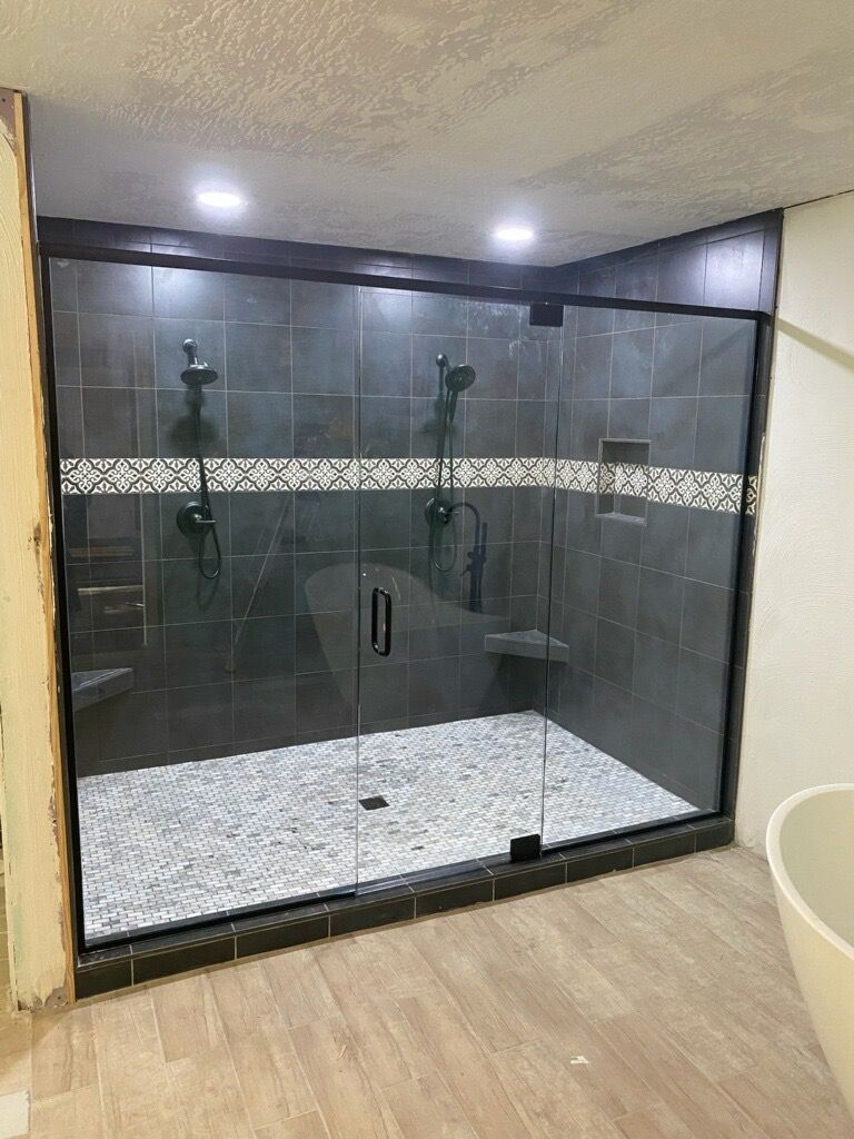 Modern tiled walk-in shower with glass doors, dark gray walls, mosaic accent strip, and white pebble floor.
