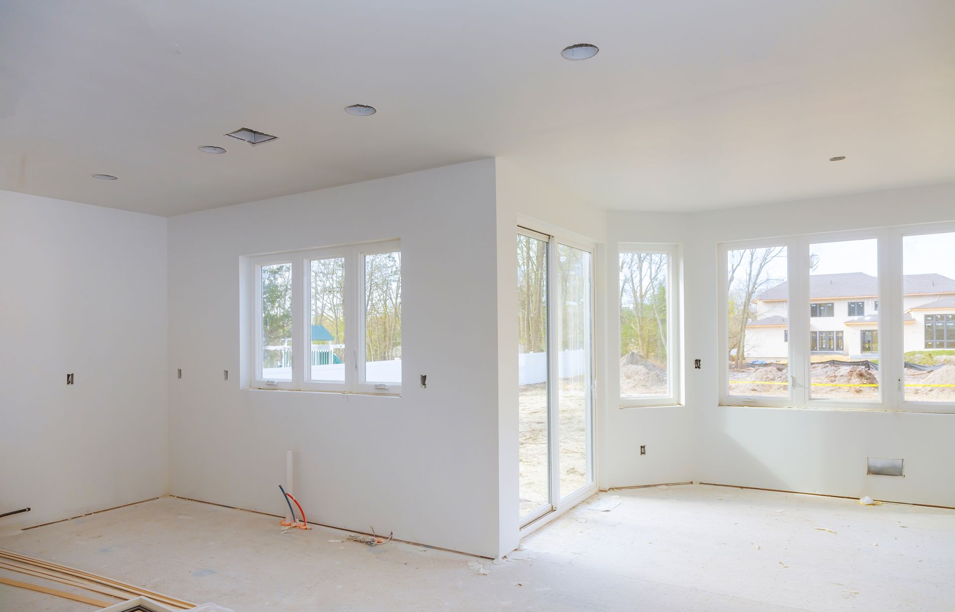 Empty room with white walls, windows, and concrete flooring in construction.