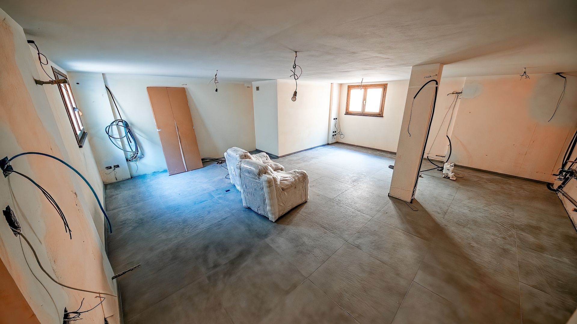 Empty unfinished basement with concrete floor, exposed pipes, and a small window letting in daylight