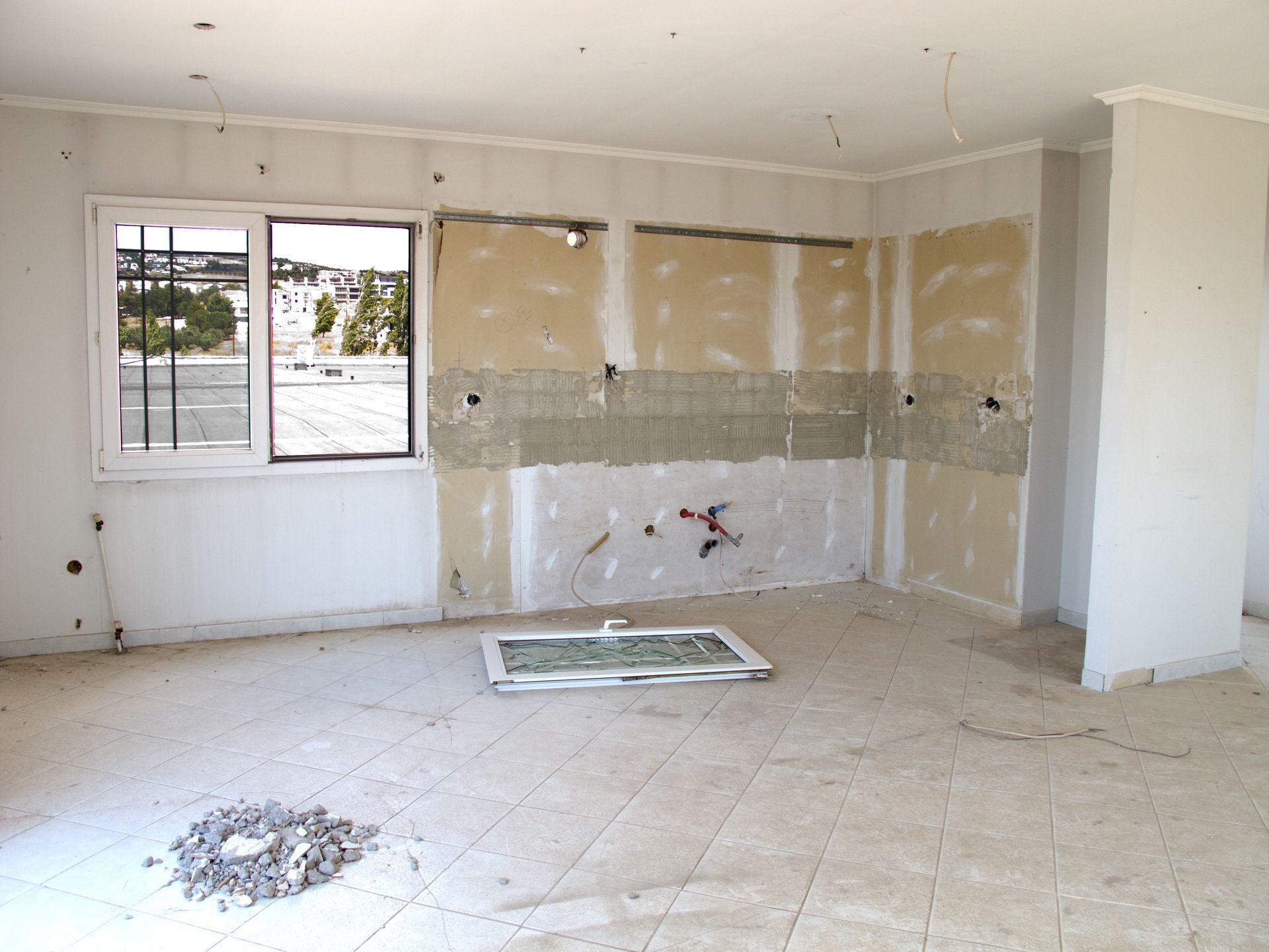 Interior room under construction; exposed walls, window, debris on floor, white walls.