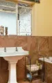 A bathroom with brown tile walls, a white pedestal sink, a bathtub, a grey storage cabinet, and a window with a metal grill.