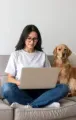 A person sits cross-legged on a sofa, working on a laptop with two golden retrievers nearby in a bright, modern room.