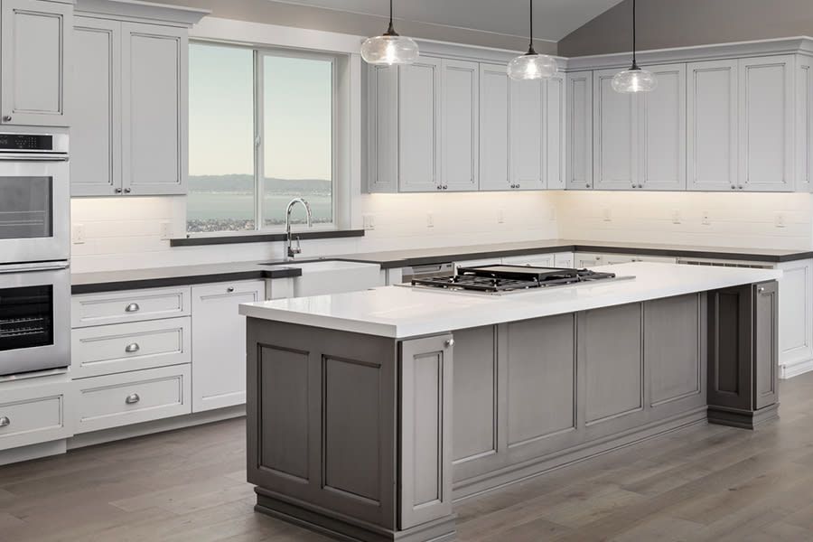A modern kitchen with white upper cabinets, a large gray central island with a built-in stovetop, and hardwood floors.