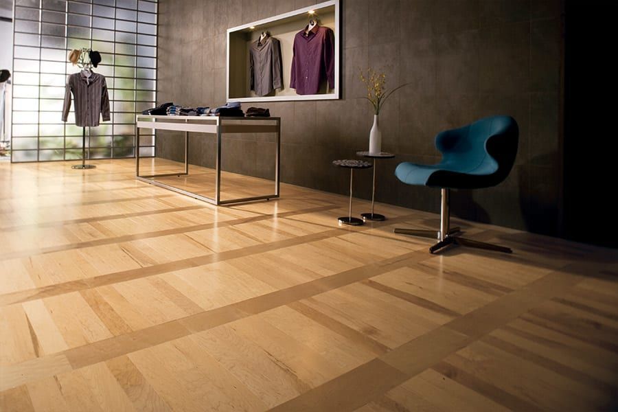 A modern clothing store interior featuring light wood flooring, a metal display table, wall-mounted shirts, and a teal chair.