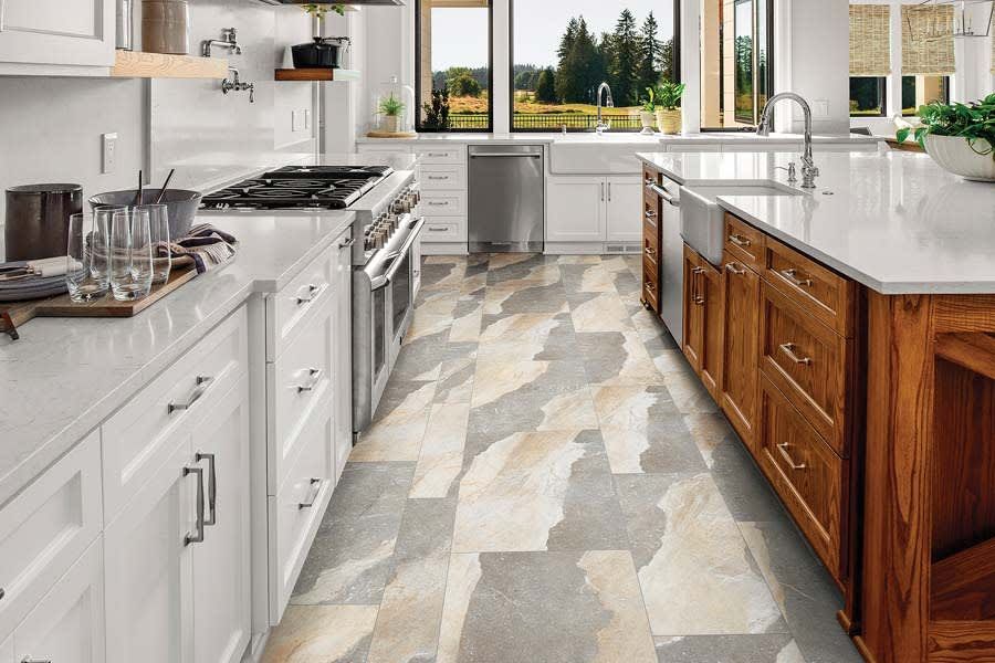 Modern kitchen with white and wood cabinets, a large island, and unique stone flooring with white, grey, and tan tones.