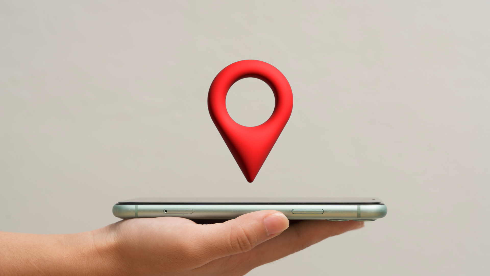 A hand holds a smartphone with a large red 3D location pin icon hovering just above the screen.