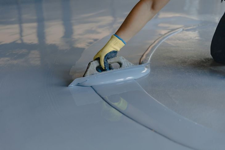 Gloved hand smoothing gray coating across a floor seam with a trowel