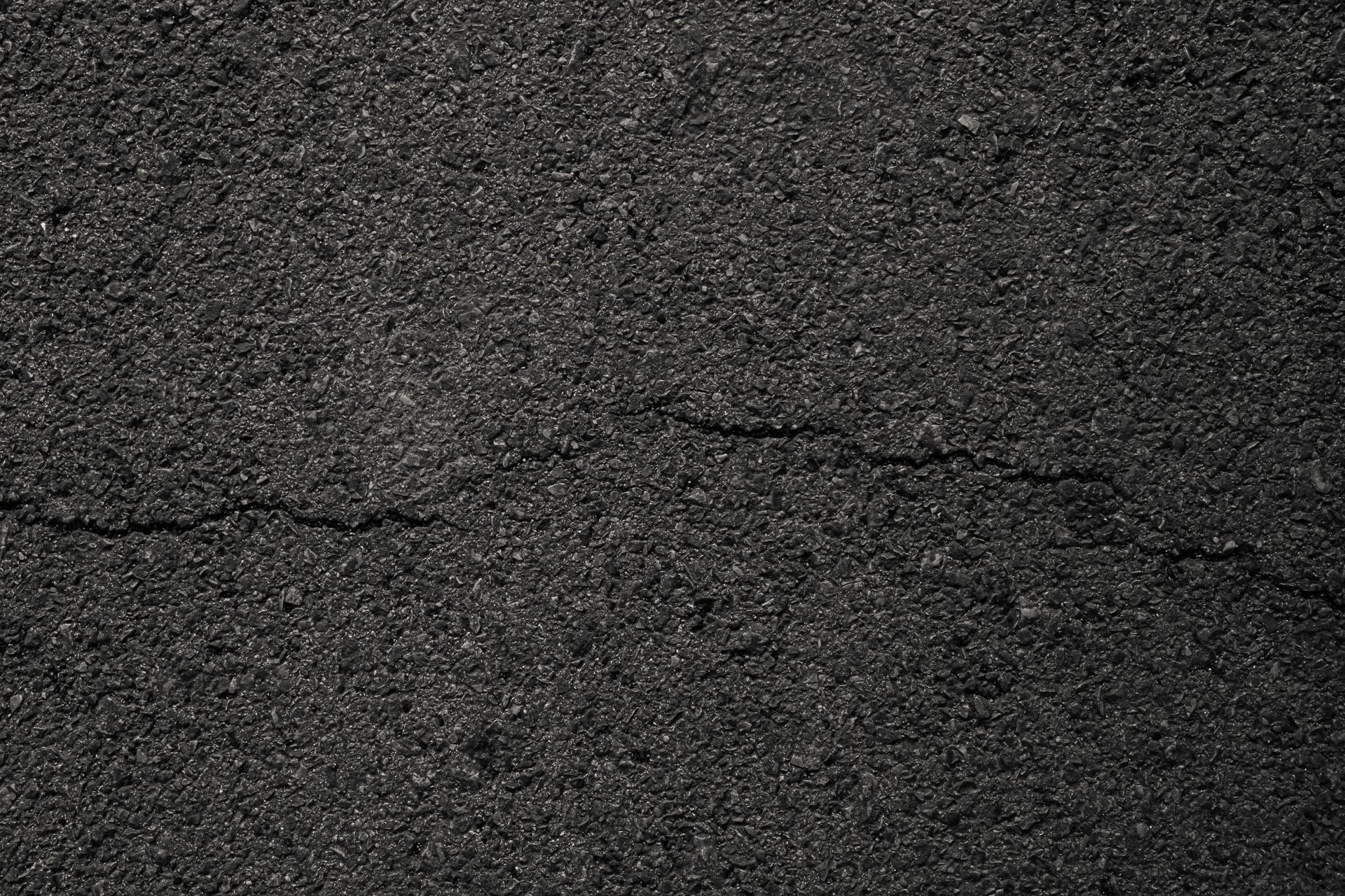 Close-up of cracked dark asphalt pavement with a horizontal fissure