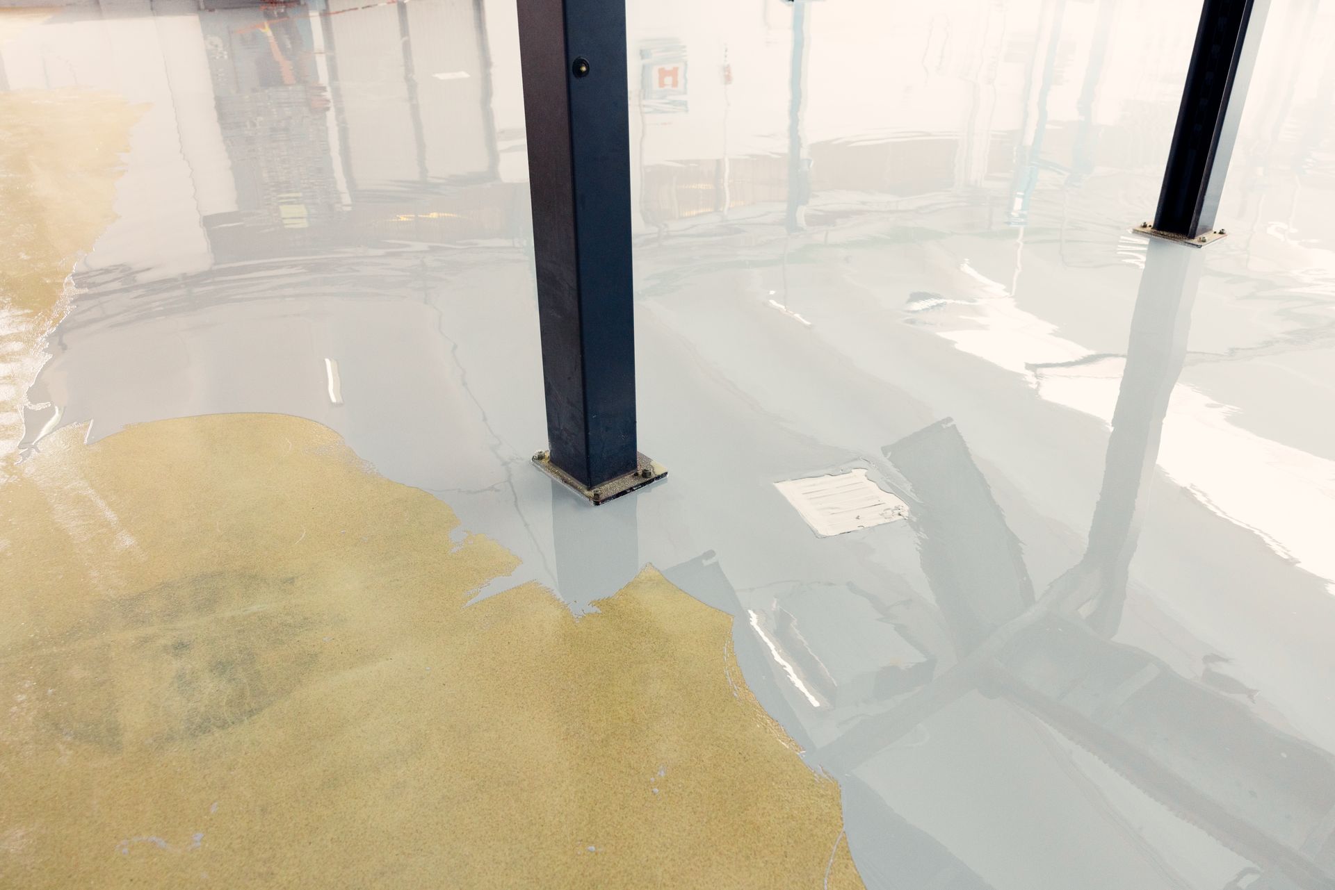 Shiny epoxy floor with wet patches and blue support columns in a bright industrial interior