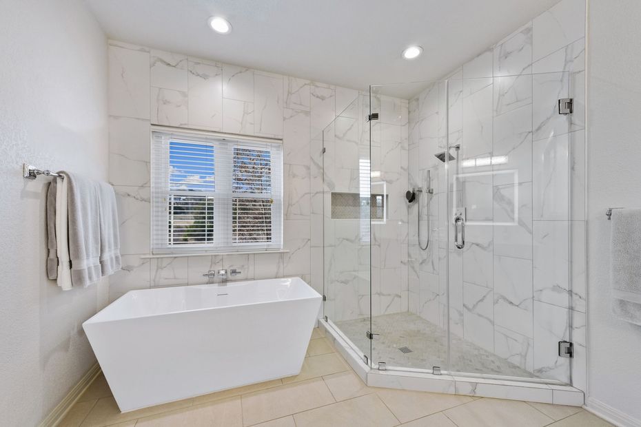 Bright white modern bathroom with freestanding tub, glass shower, marble walls, and window shutters