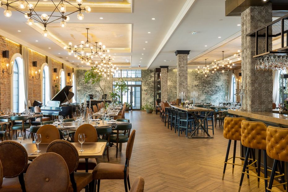 Elegant restaurant interior with chandeliers, warm lighting, tables, chairs, and a long bar counter