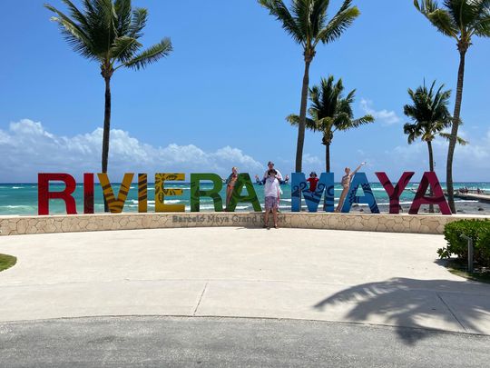 A family stands in front of a sign that says riviera maya