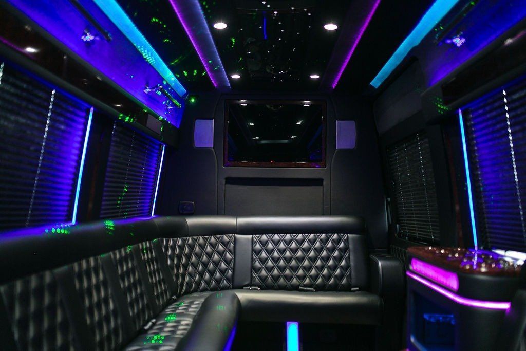 Inside of a black party bus with black leather seating and colorful neon lights.