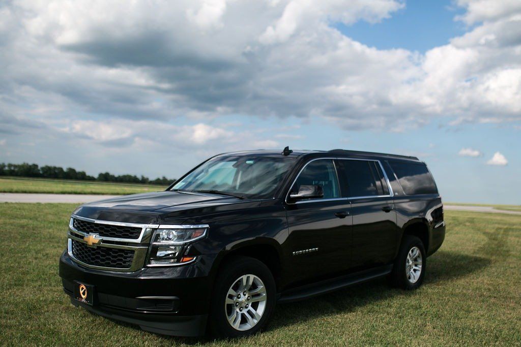 Black Chevrolet Tahoe SUV on grass field, with a blue sky and clouds.