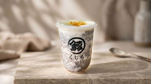 Clear plastic cup of iced milk tea with whipped topping on a table, blurred spoon in the background