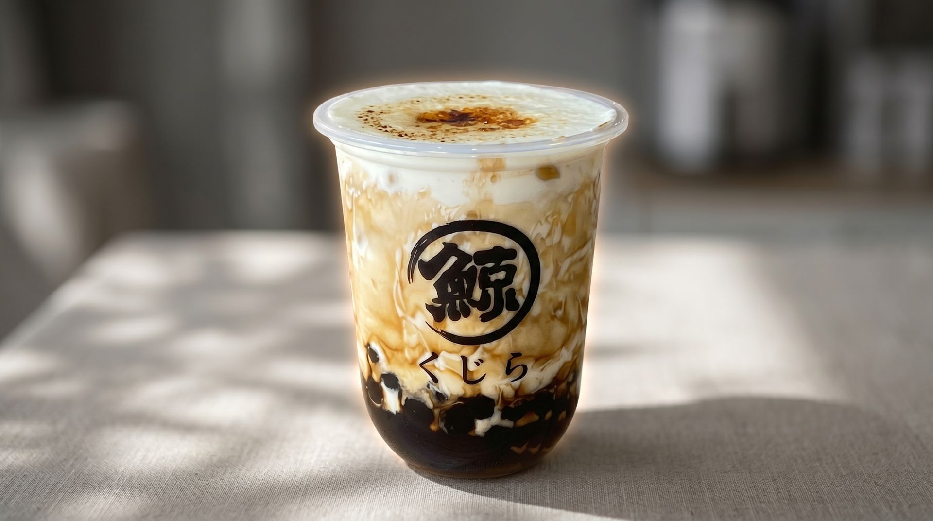 A clear plastic cup of iced bubble tea with dark tapioca pearls on a sunlit table