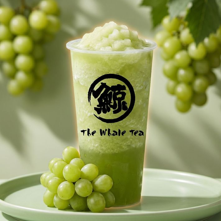 Green grape slush drink in a clear cup on a plate, with grape clusters in the background