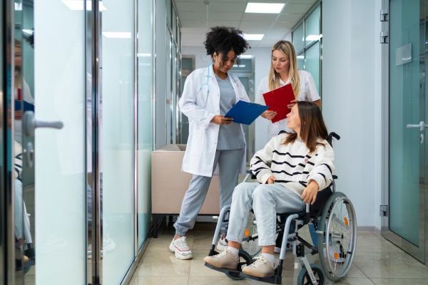 A woman in a wheelchair is talking to two doctors in a hospital hallway.