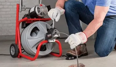 Man wearing gloves working with a machine to fix drai