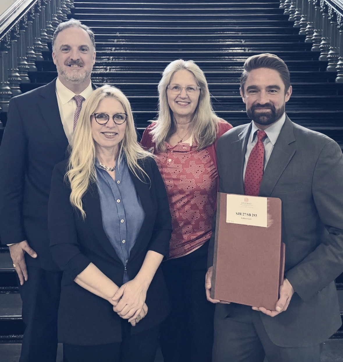 Three people stand in a line with Jennifer Lundy on a staircase for the passage of SJR27/SB293