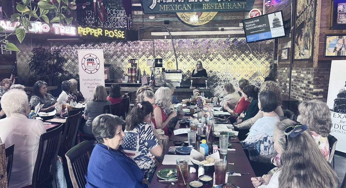 A group of people sitting at a long table in a restaurant setting, attending a meeting or presentation.