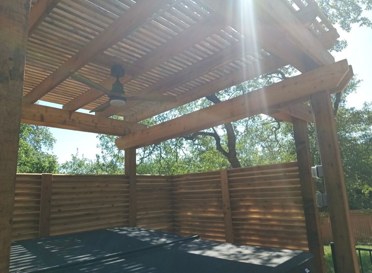 A wooden pergola with a ceiling fan on top of it