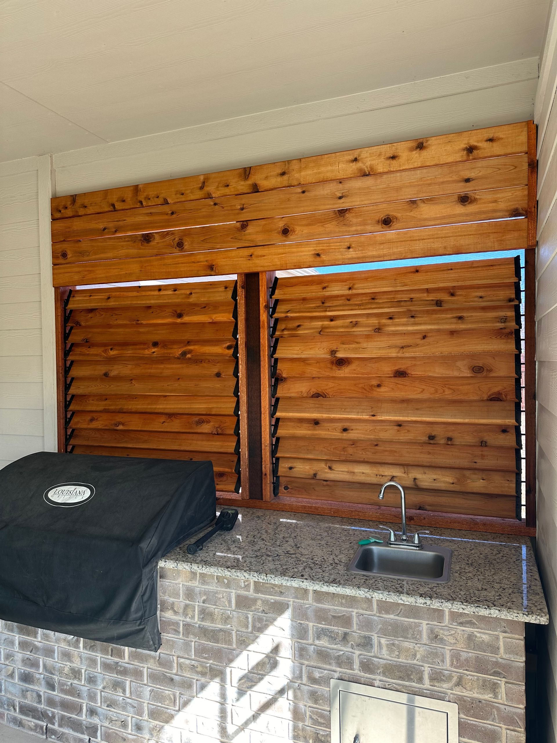 A kitchen with a grill , sink and wooden shutters.