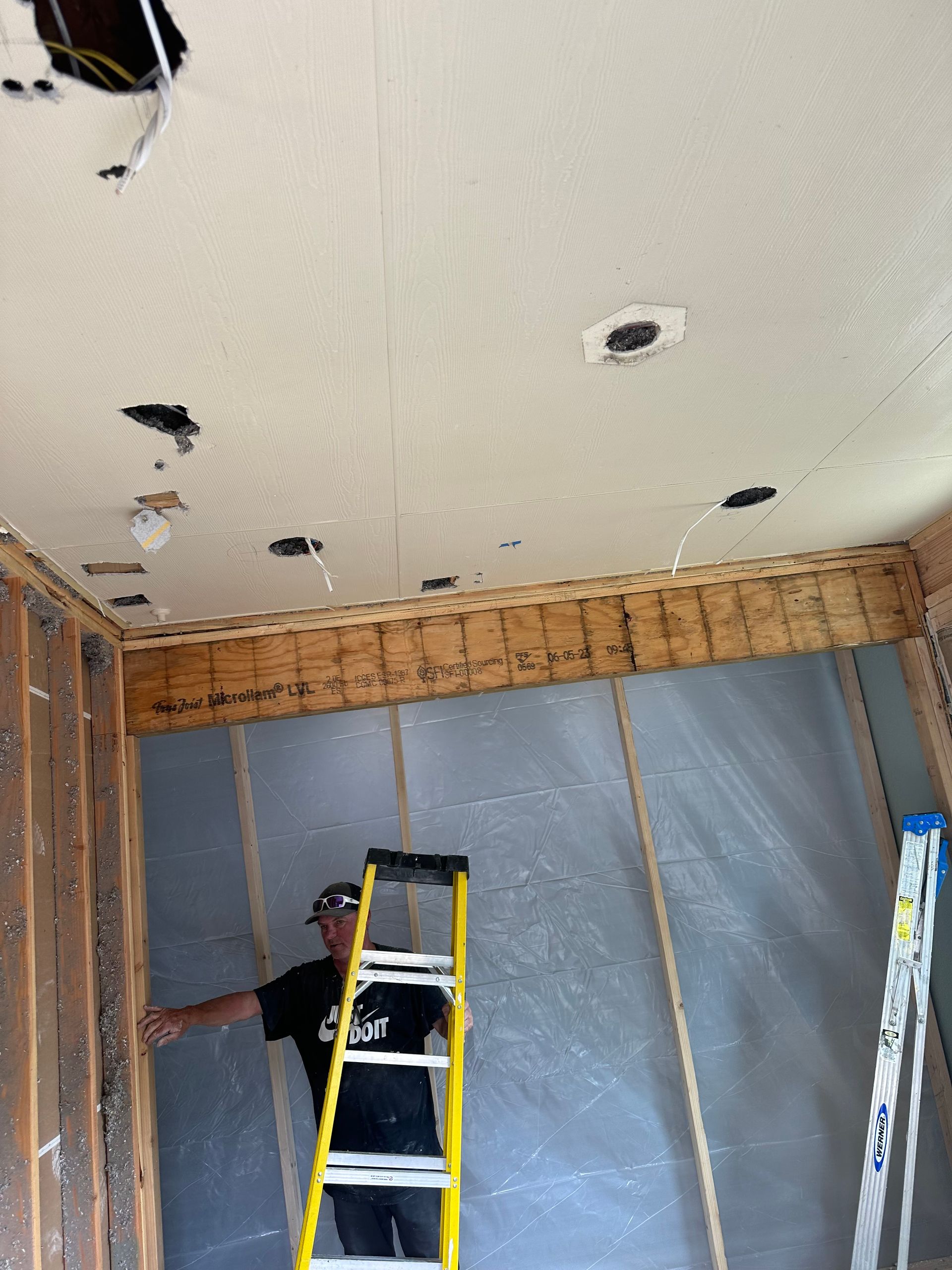 A man is standing on a ladder in a room under construction.