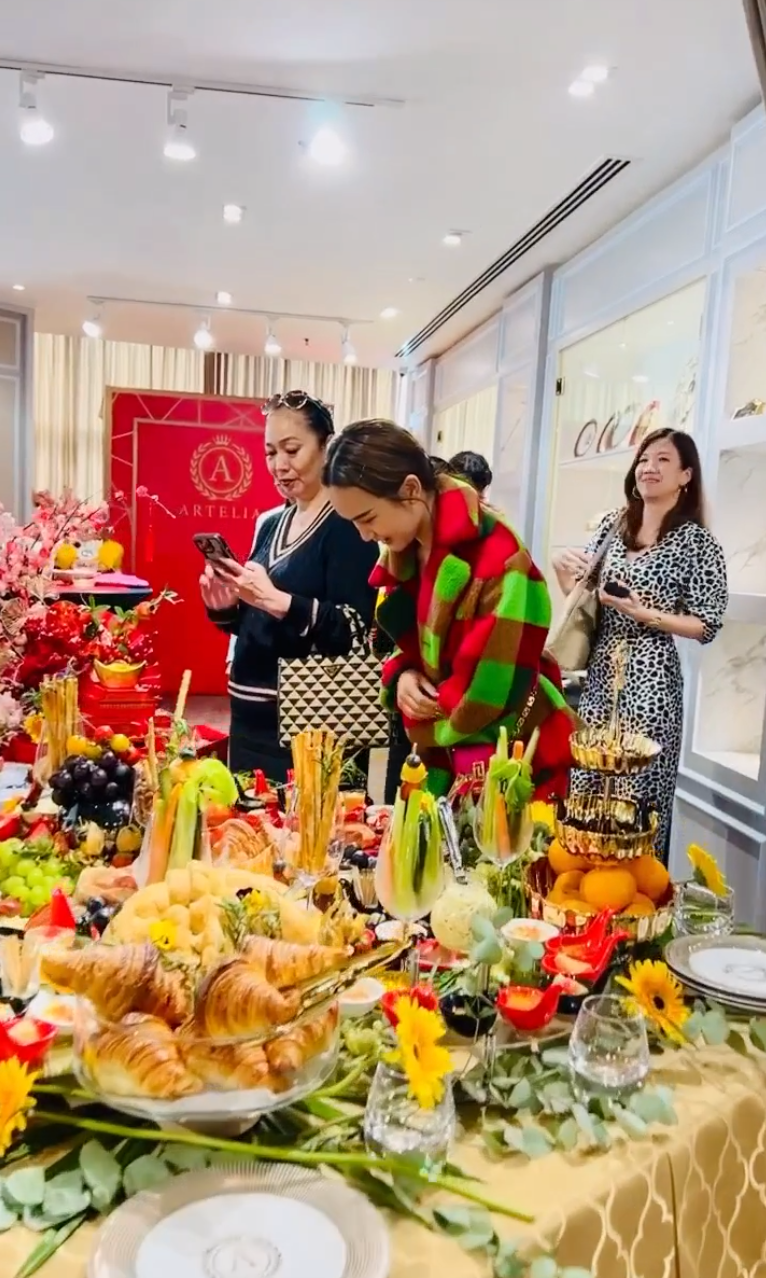People gathered around a decorated food table at a festive indoor celebration, with fruit and snacks displayed.