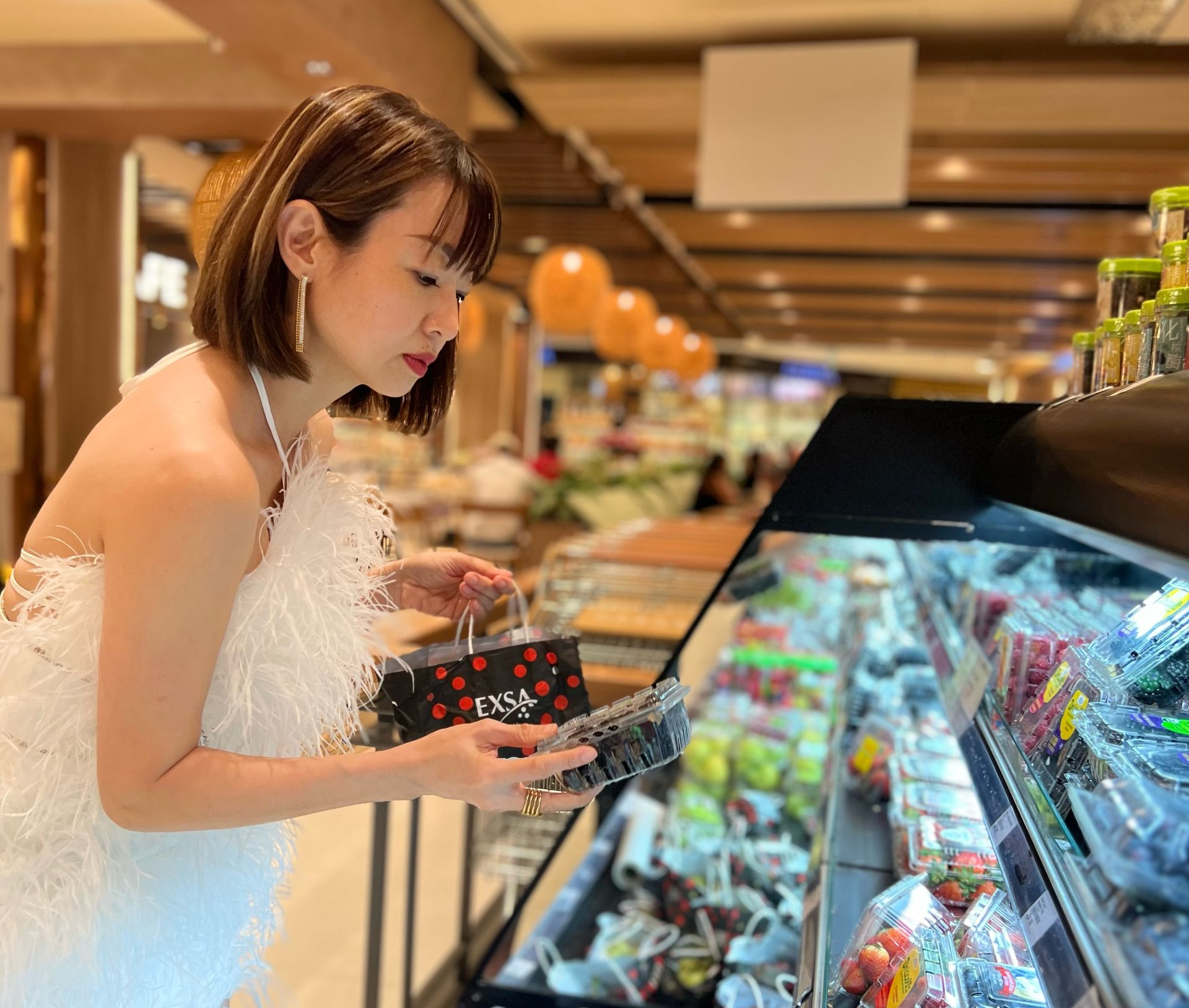 Woman in a white dress choosing packaged goods at a supermarket deli counter