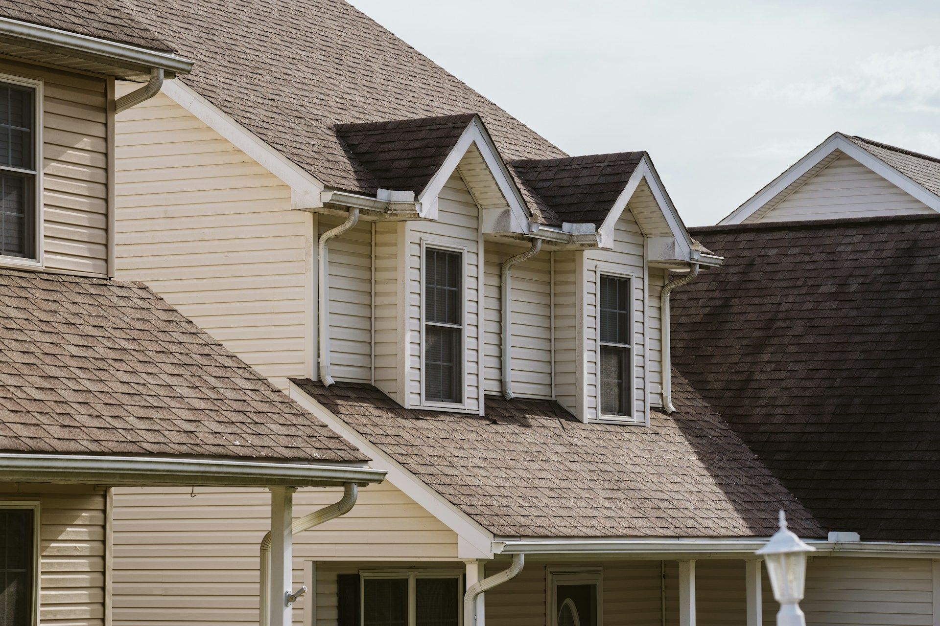 Suburban house roof with beige siding and multiple dormer windows