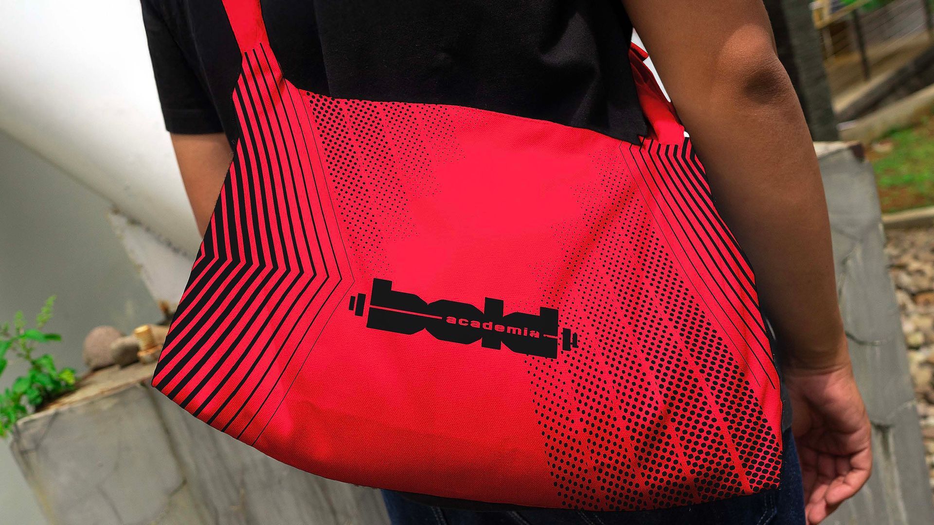 Bolsa de ombro vermelha e preta com estampa listrada, usada por uma pessoa ao ar livre.