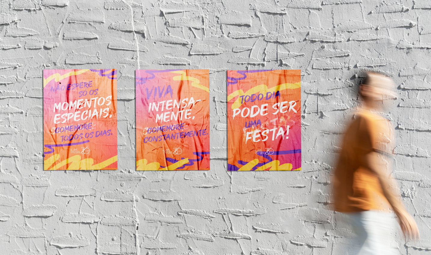 Três cartazes coloridos em uma parede de tijolos brancos; uma pessoa desfocada caminha à direita. Os cartazes têm desenhos em laranja e roxo com texto em português.
