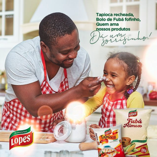 Adulto e criança cozinhando juntos em uma cozinha, sorrindo ao lado dos produtos de farinha de tapioca Lopes.
