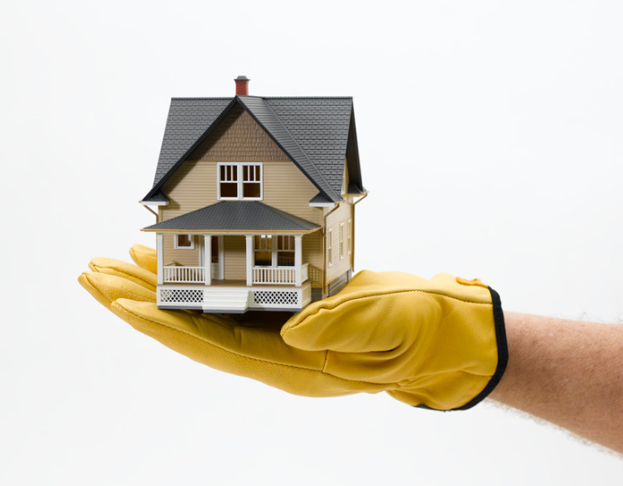 Hand in yellow glove holding a miniature house, isolated on white.