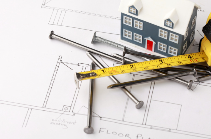 Floor plan with miniature house, nails, and a measuring tape, suggesting construction or renovation.