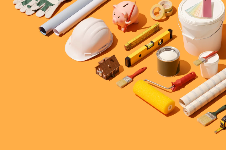 A flat-lay view of home renovation tools including a hard hat, paint rollers, brushes, and a miniature house model.