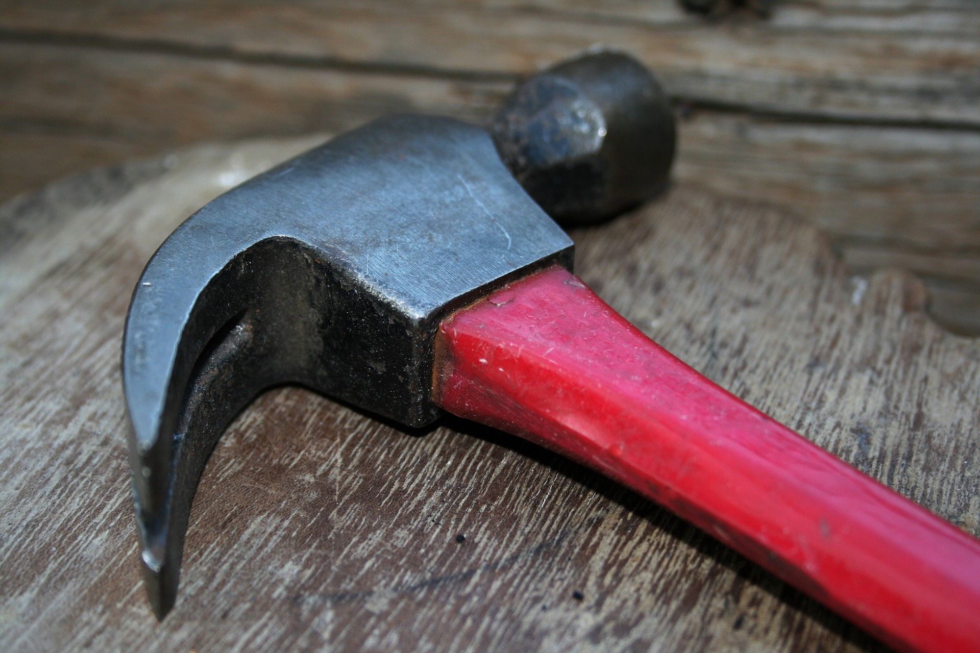 Red-handled claw hammer on a wooden surface, showing the claw, head, and part of the handle.
