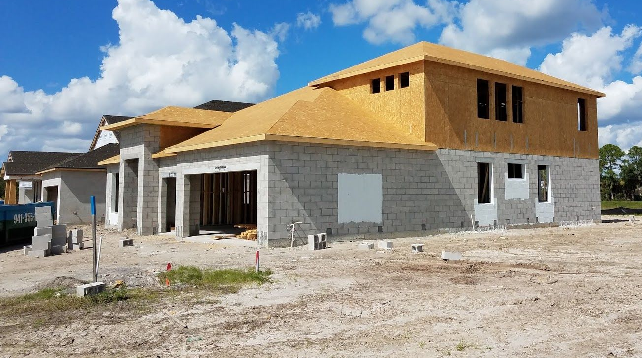 A new house under construction featuring concrete block walls, wooden roof sheathing, and a large garage opening.