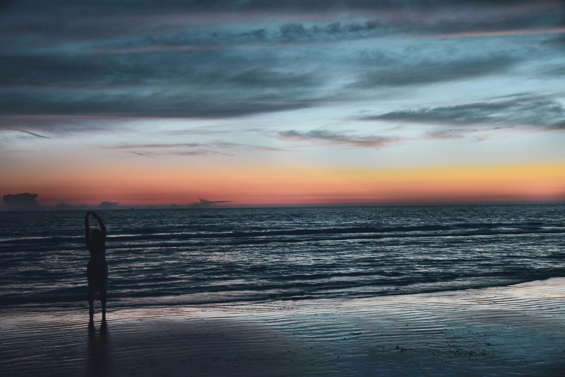 Silhouette of a person at a beach during a colorful sunset over calm water