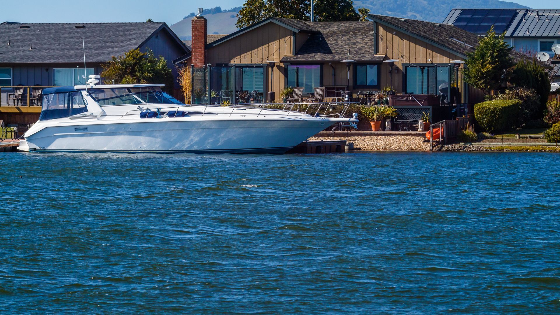 White yacht on blue water in front of waterfront houses on a sunny day