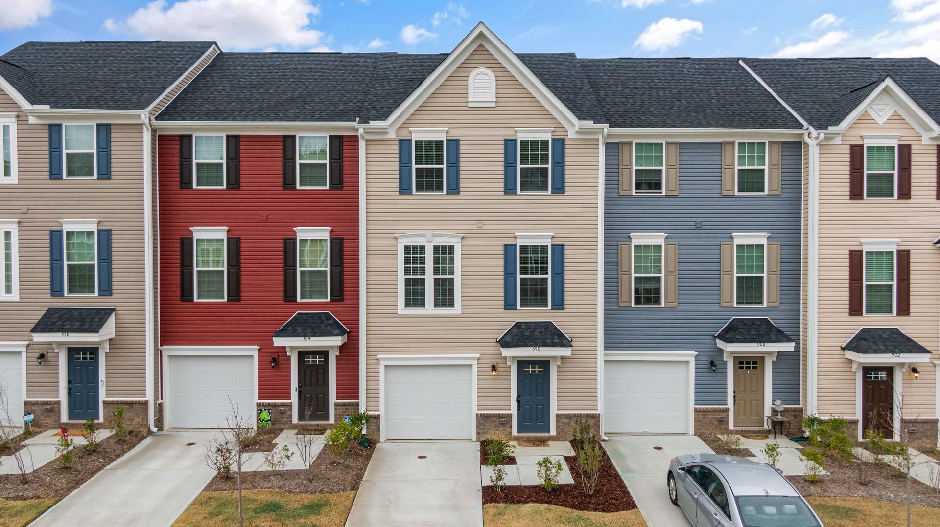 Row of colorful townhouses with garages and driveways under a partly cloudy sky