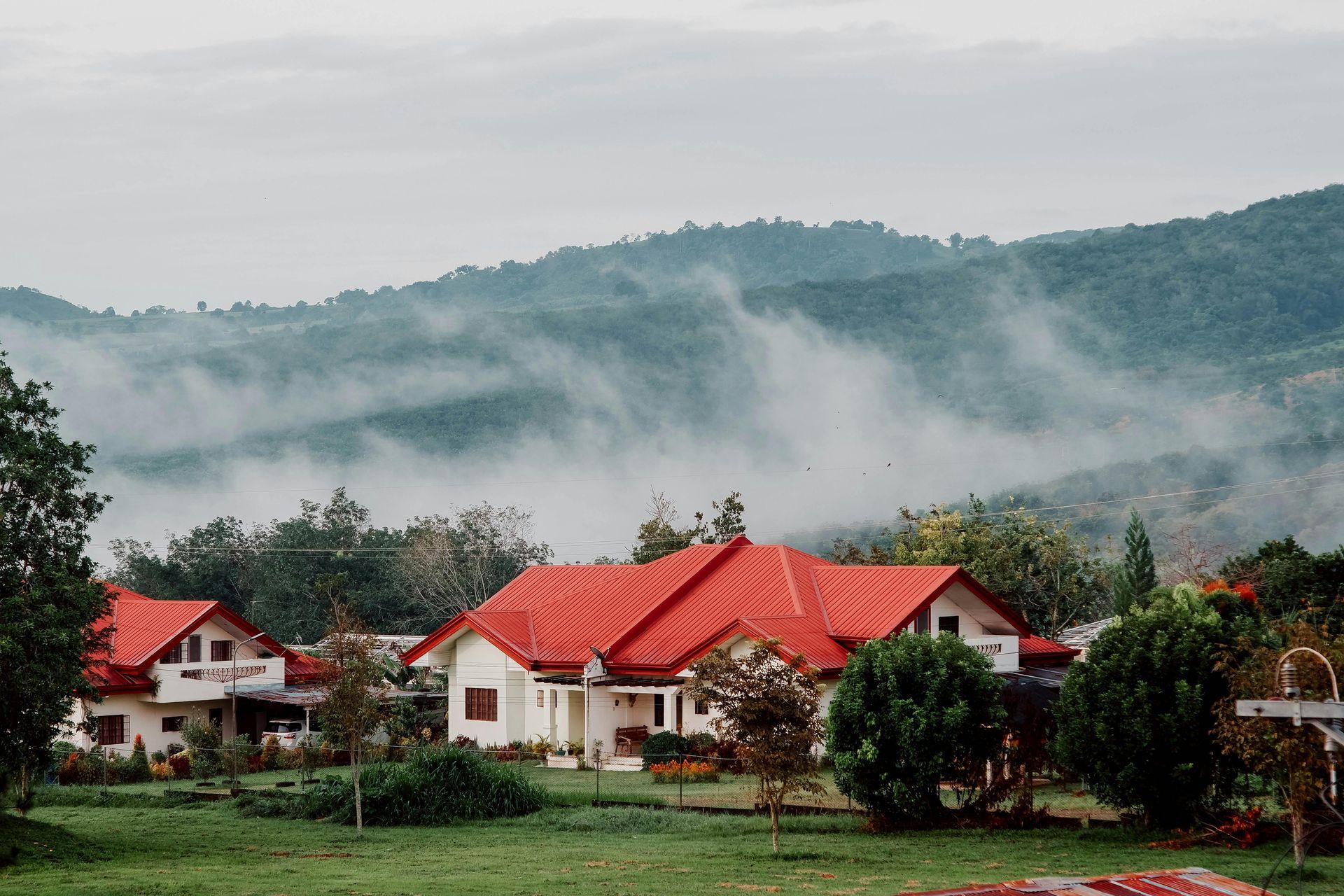 Red-roofed houses in a misty green valley with forested hills in the background