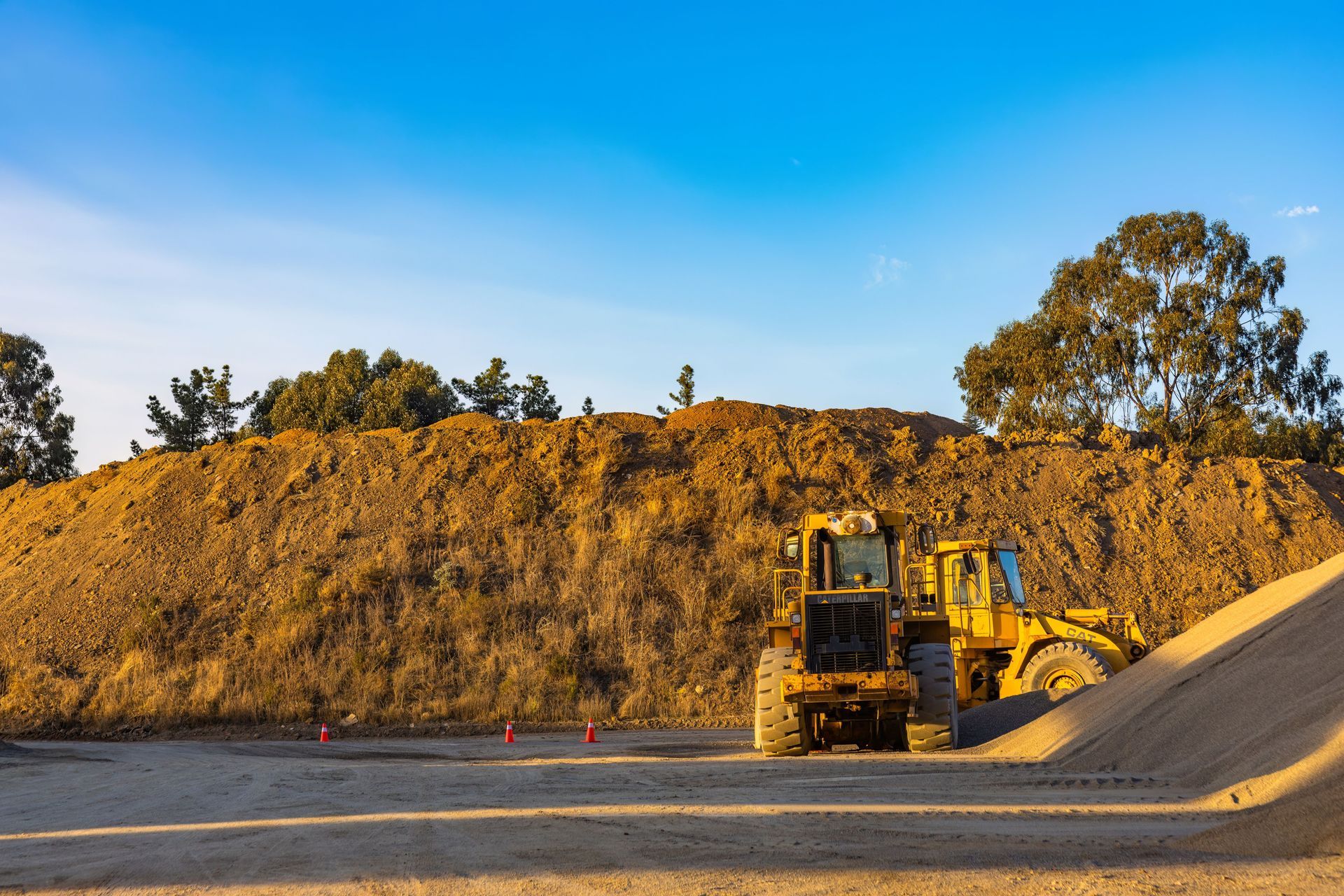 Yellow excavator beside a dirt mound at a construction site under a clear blue sky
