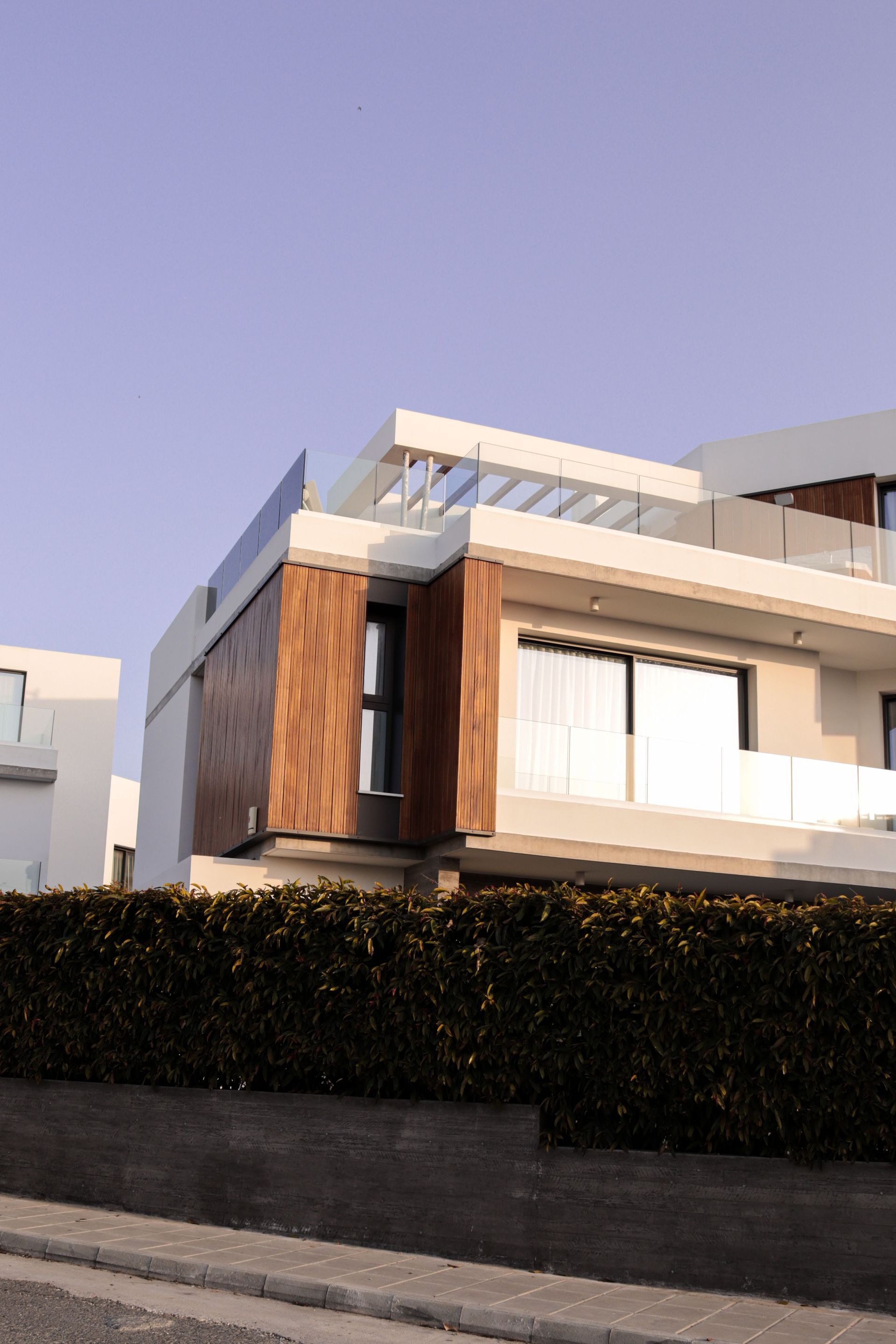 Modern house with white and wood exterior behind a hedge under a clear purple sky